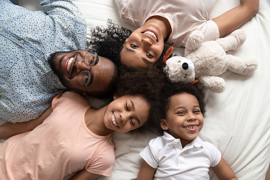 Client Center - Smiling Parents With Their Two Kids Laying In Bed